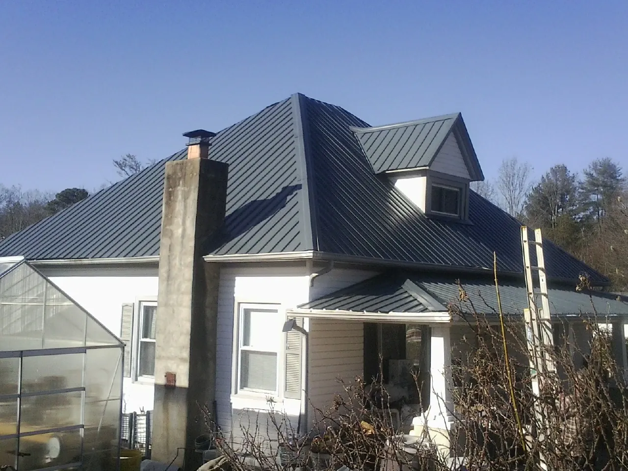 Dark blue standing seam metal roof on a white farmhouse with dormer — Slate & Tile Roof Repair by Roofing Brothers in Porter