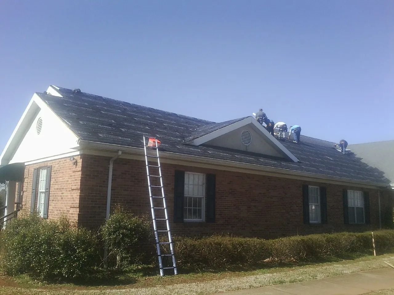 Crew tearing shingles off a brick ranch roof with a ladder set — Emergency Roof Repair work by our crew in Porter