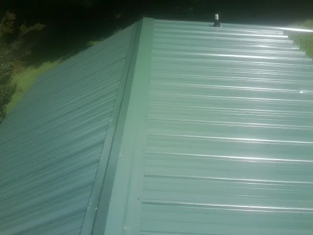 New green metal panels meeting at the ridge of a roof — Flat Roof Repair work by our crew in Porter