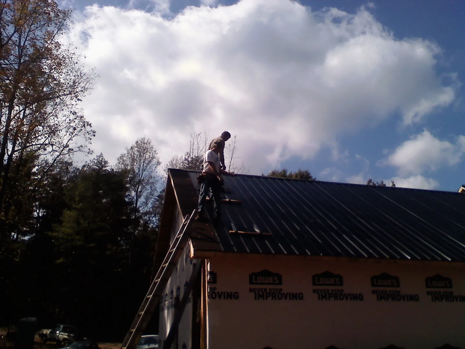 Roofer fastening dark metal panels high against a cloudy sky, from a Roof Inspection job in Porter