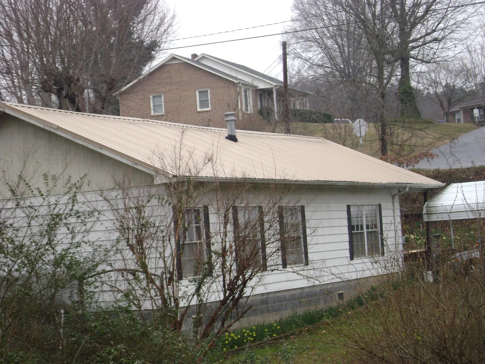 Tan metal roof on a white sided house set into a hillside — Commercial Roofing by Roofing Brothers in Porter
